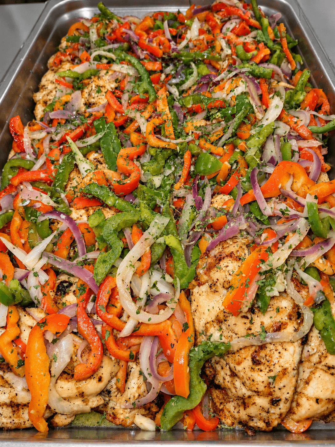 Seasoned chicken with sweet peppers, onions, and herbs in a catering tray
