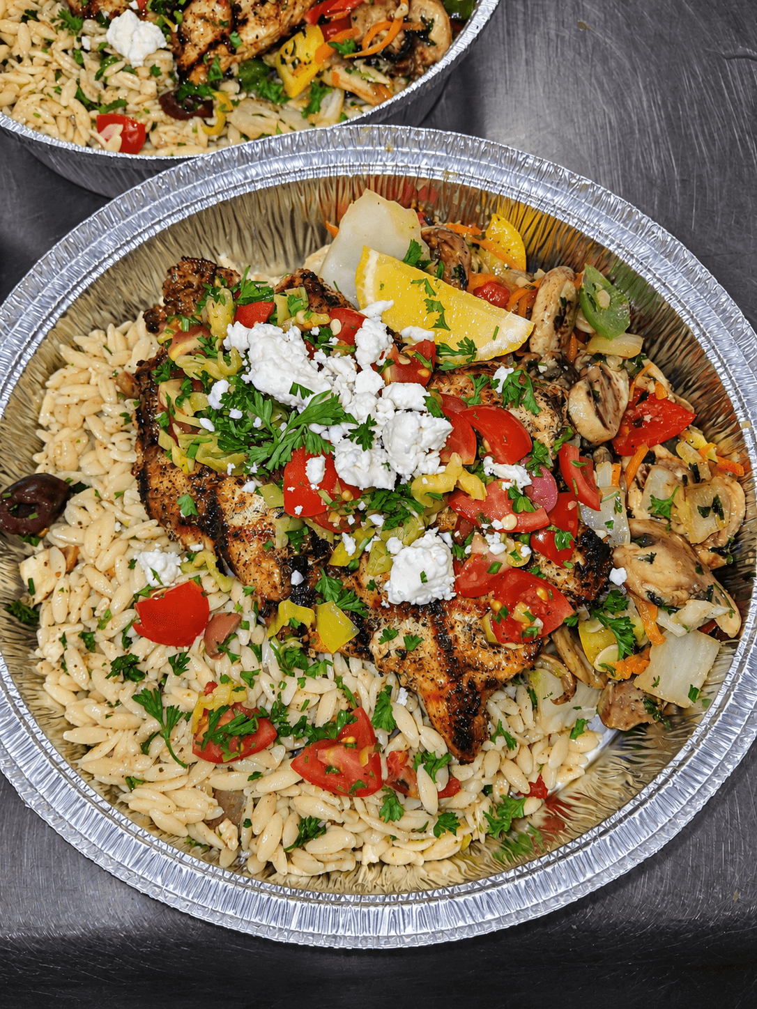 Grilled chicken served with orzo, vegetables, and crumbled cheese in a catering pan